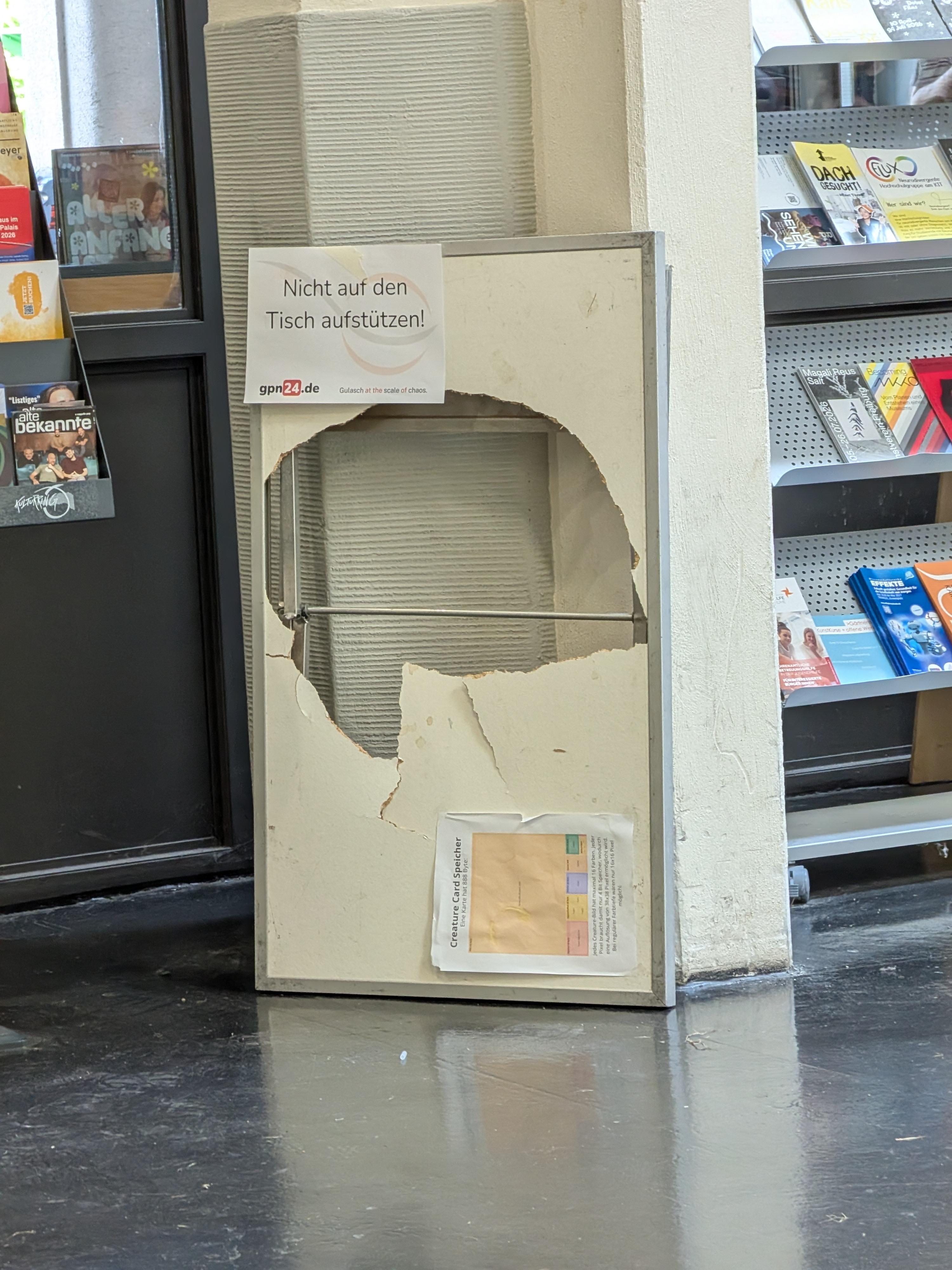Picture of an upgright standing desk with a sign that says you shouldn't put your weight on it. The table has a large hole in the middle